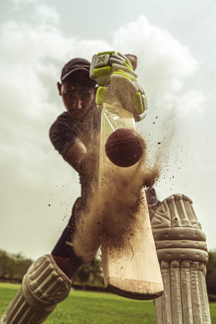 Cricketer in motion striking the ball with intense focus, clouds of dust captured.