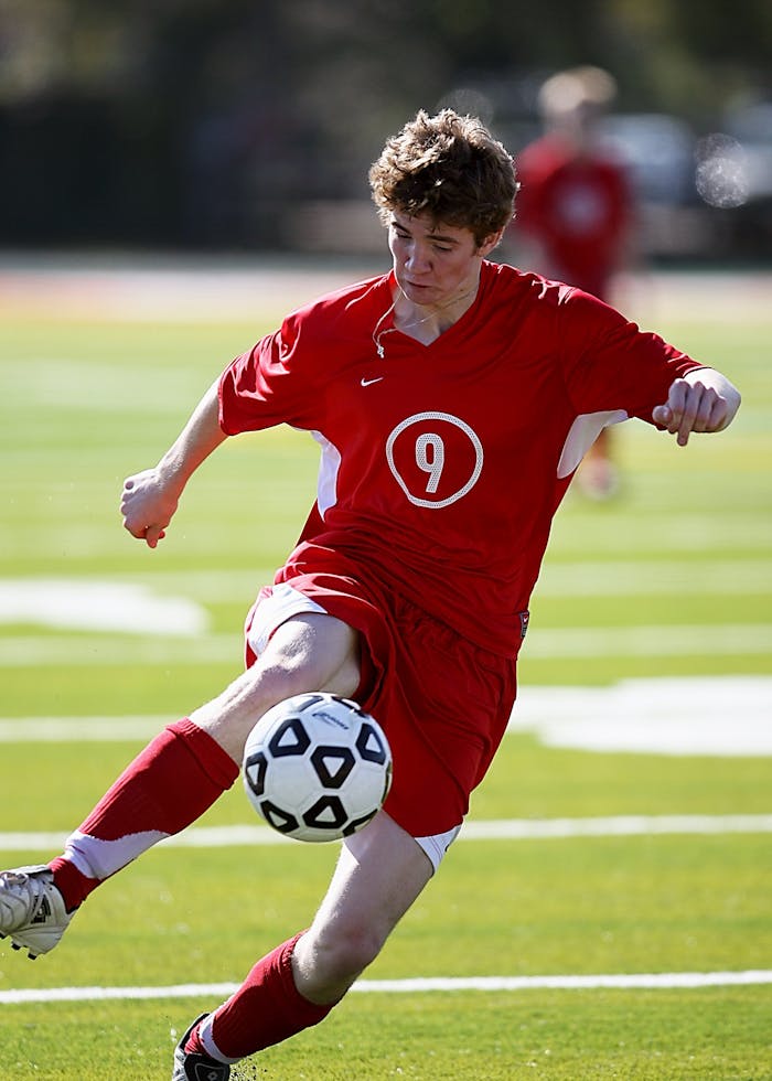 Soccer player in red uniform kicking ball during a match outdoors.